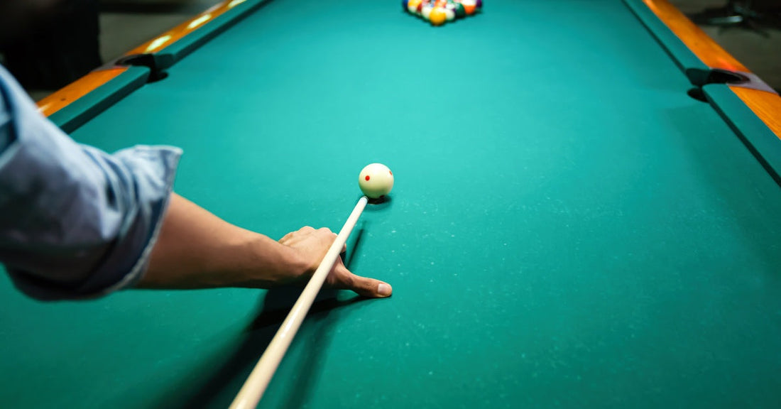 Someone lining up their break shot. The cue ball is in position and the rest of the balls are racked up at the end of the table.